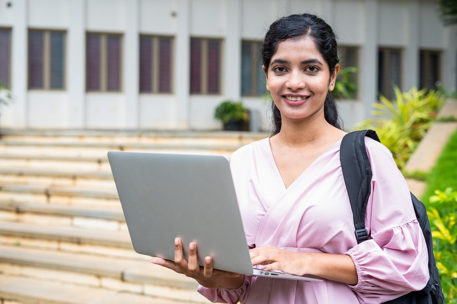 An Indian student holding a laptop on a college campus